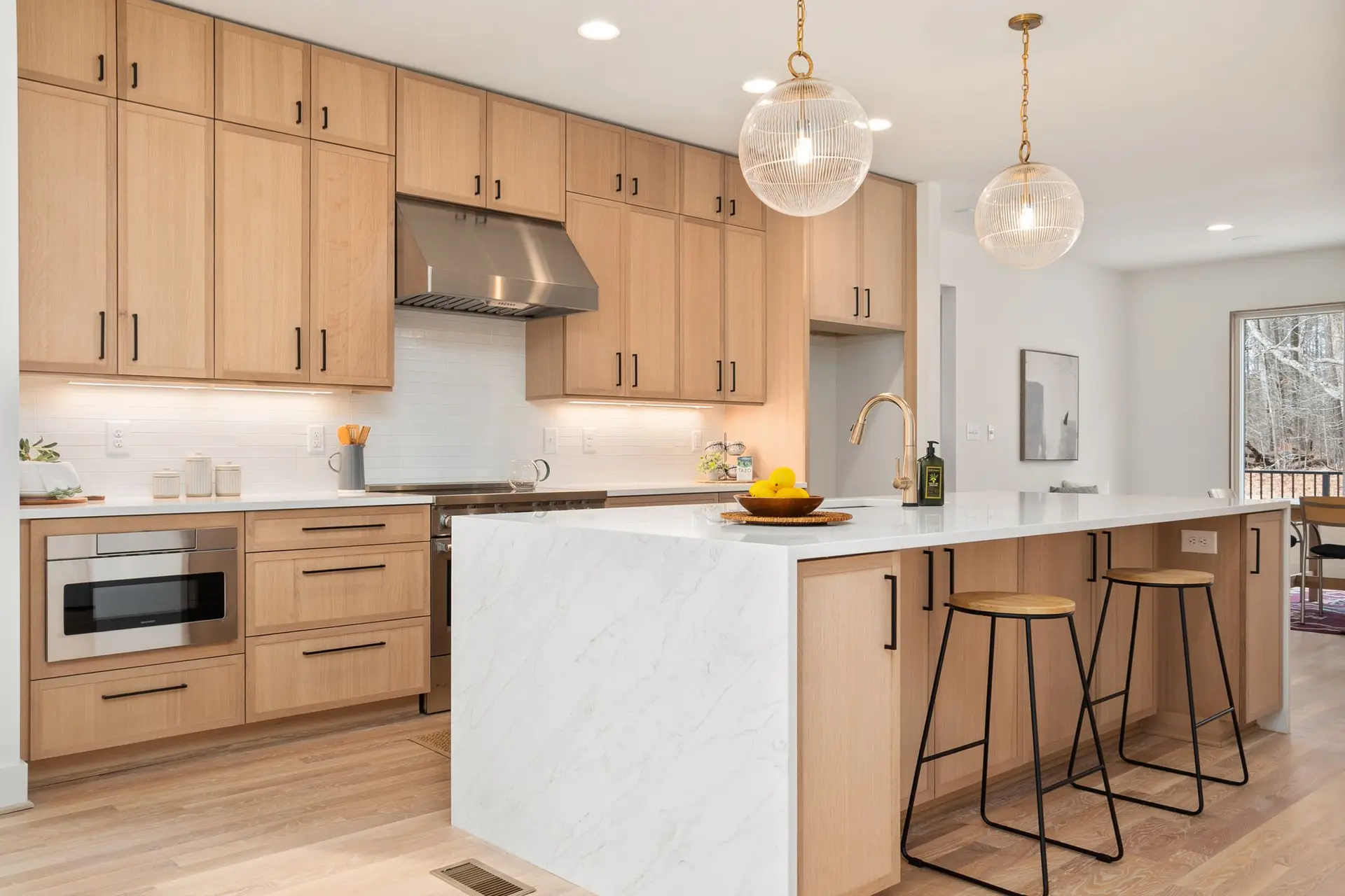 Cocina con muebles de madera clara, isla con encimera blanca y taburetes