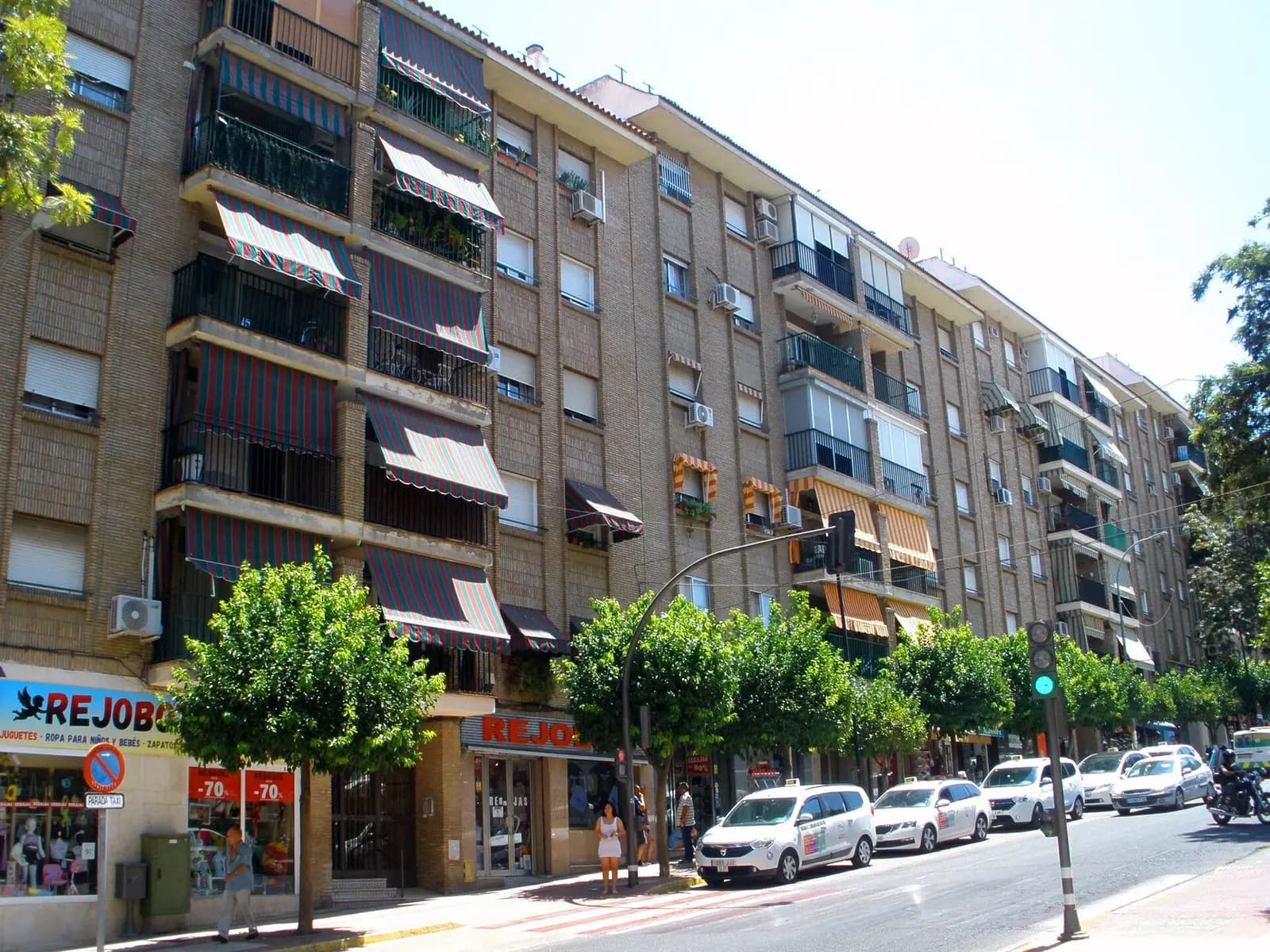 Bloque de pisos de ladrillo visto de cinco plantas con toldos de rayas en los balcones, aparatos de aire acondicionado en fachada y comercios en la planta baja