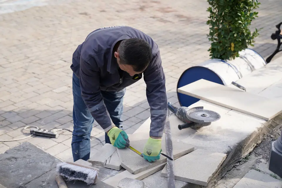 Operario con guantes midiendo y marcando una baldosa antes de cortarla